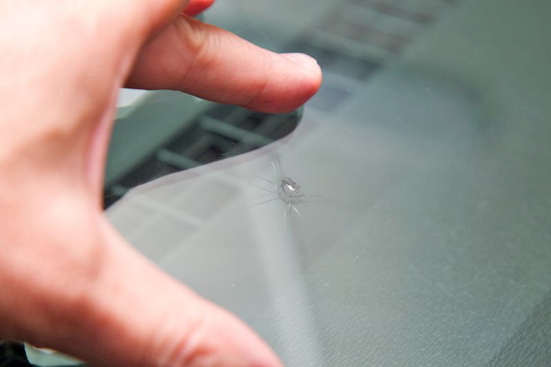 A closeup of an anonymous person touching a chip in a car windshield that has started to spider.