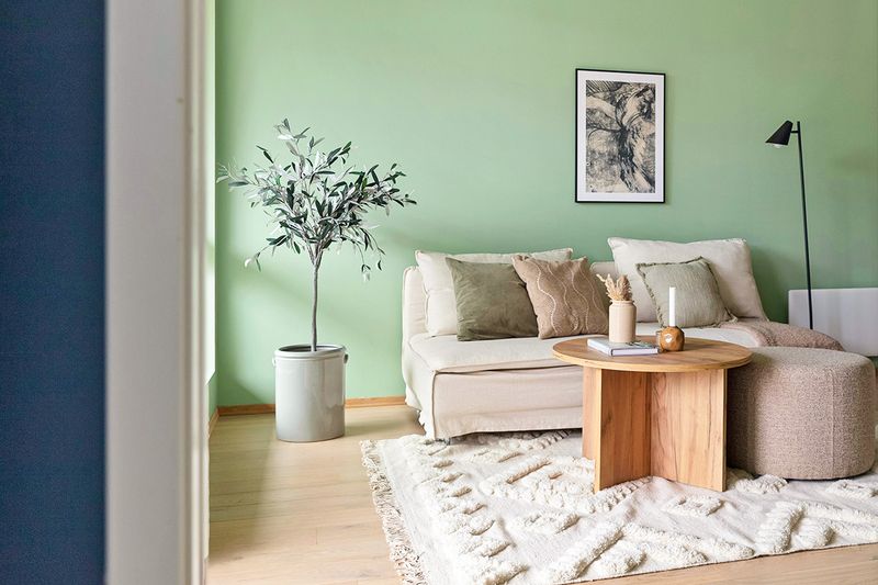 A living room with pistachio-colored walls, neutral furniture, and light wood floors.