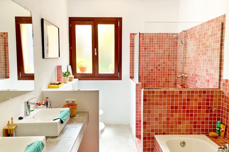 This modern bathroom features a red square tile shower surround, a concrete vanity, and bathroom essentials on every flat surface.