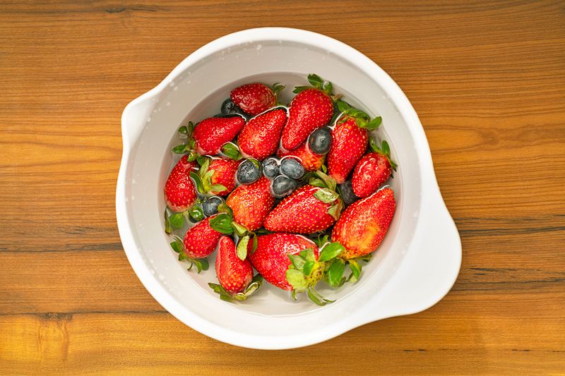 Mixing bowl full of water, vinegar, strawberries, and blueberries.