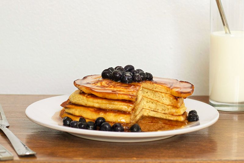 A short stack of pancakes covered in blueberries and syrup with a sliver cut out.