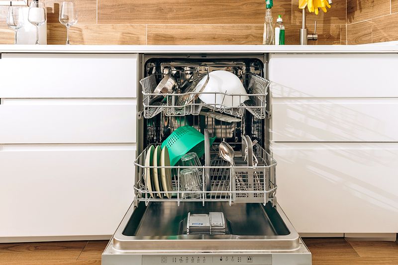 An open, loaded dishwasher in a kitchen with white cabinets and a wood-look tile backsplash.