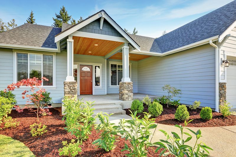 A contemporary Craftsman-style home painted light blue with wood accents and fresh landscaping.