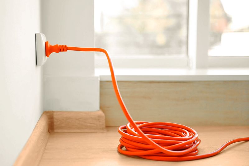 An orange extension cord plugged into an indoor wall outlet.