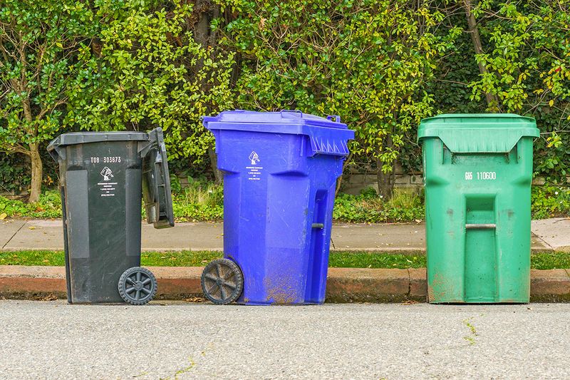 A trash bin, a recycling bin, and a green waste bin on a curb, waiting for pickup.