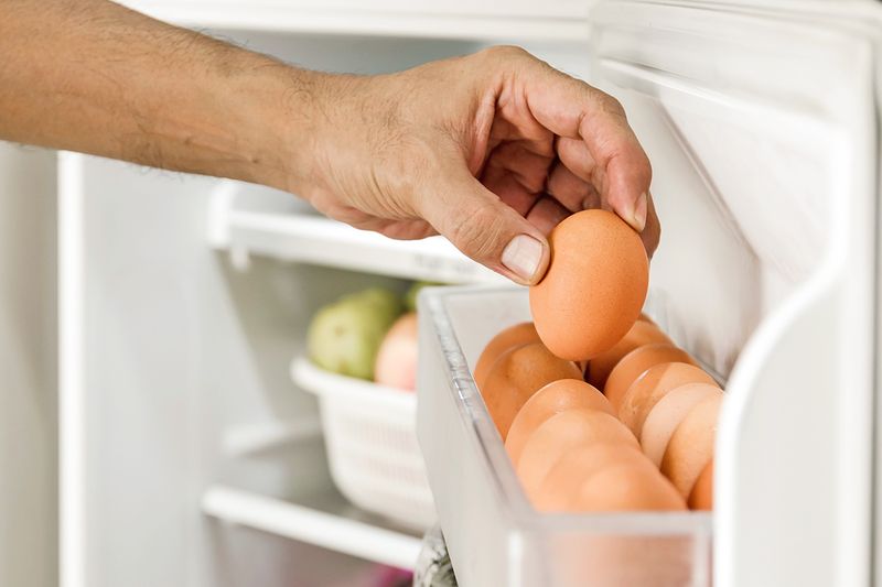 Anonymous person removing an egg from the basket in the refrigerator door.
