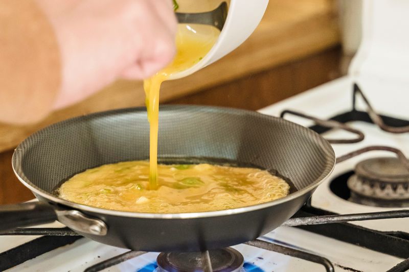 Anonymous person pouring whisked eggs into a frying pan.