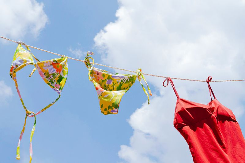 A yellow floral bikini and a red one-piece hanging on a clothes line against a blue sky.