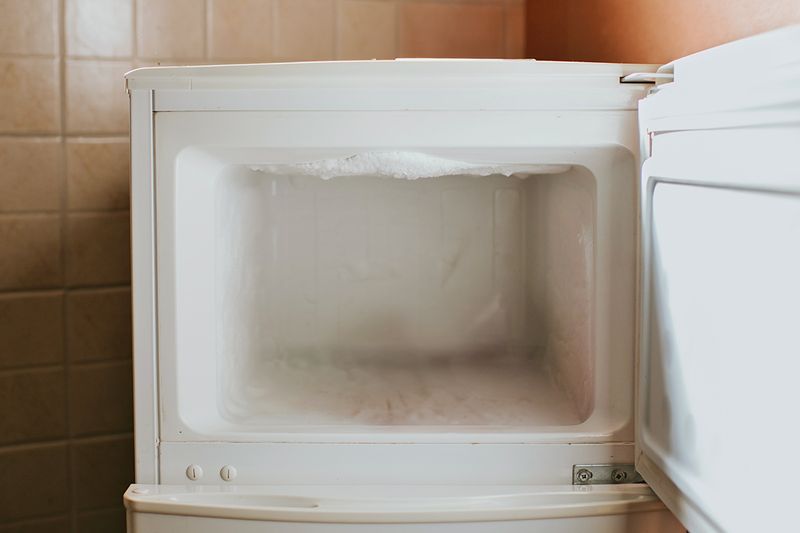 An open, empty freezer with ice buildup inside.
