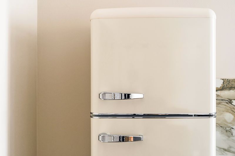 A close-up shot of an off-white, retro-style refrigerator and top freezer with chrome hardware.