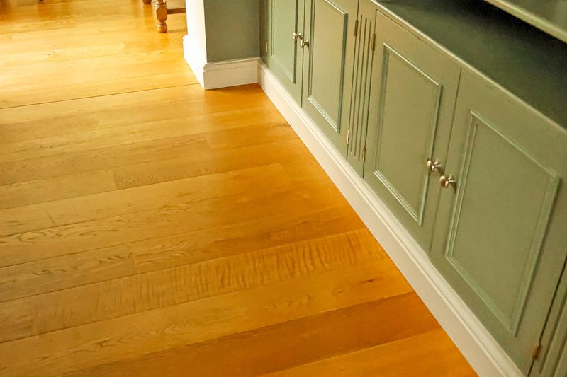 Sage green built-in cabinets with white-painted baseboards adjacent to an oak wood floor.