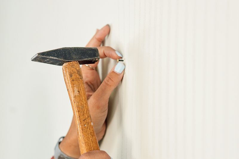 Anonymous woman hammering a picture nail into a white wall with a hammer.