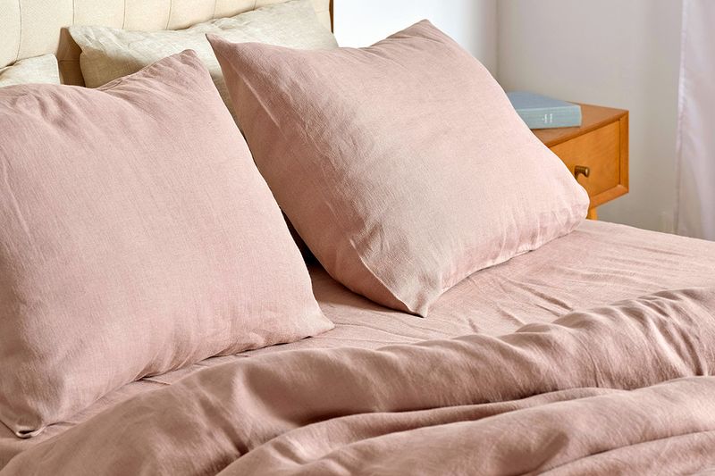 A close-up shot of a bed with light pink linen sheets and matching pillow cases.