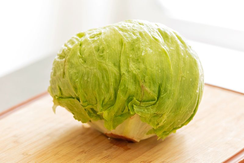 A head of iceberg lettuce on a wooden cutting board.