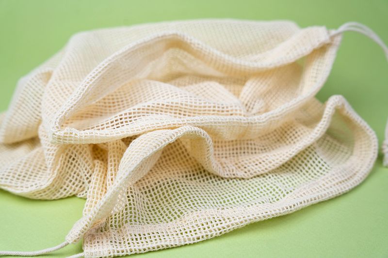An off-white mesh laundry bag against a lime green background.