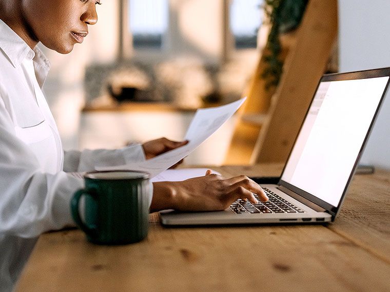 An image of a woman looking at a paper while on a laptop