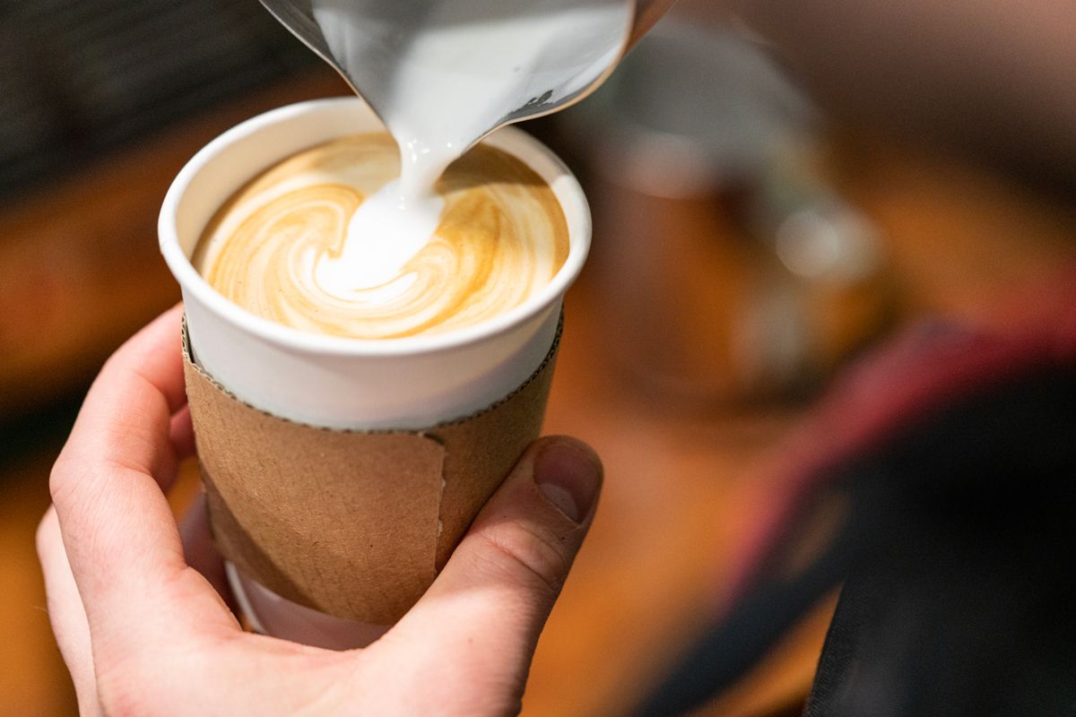 A close-up image of a barista pouring milk into a latte