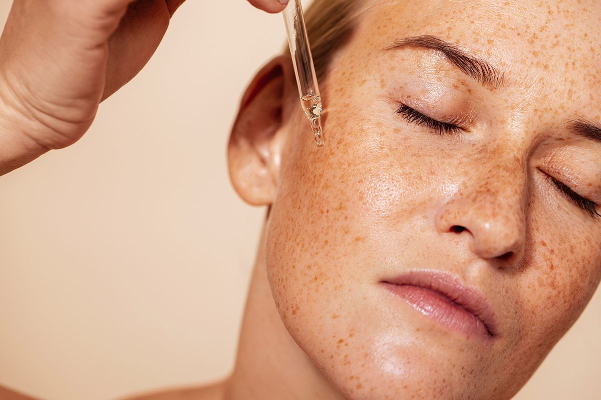 Woman with closed eyes applying face serum with pipette