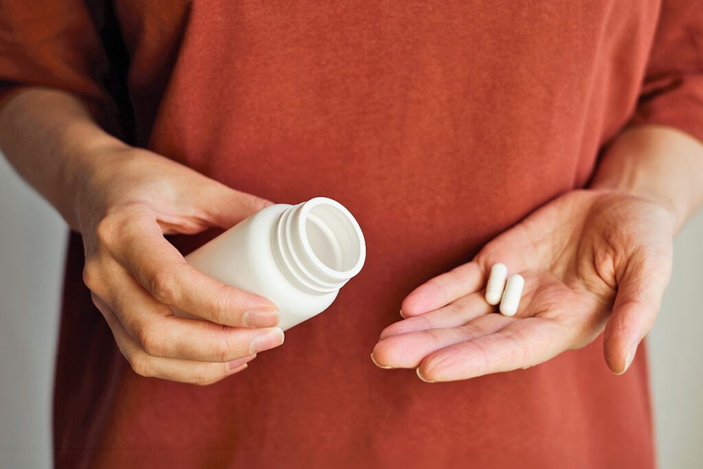 Person holding bottle in one hand and two pills in the other