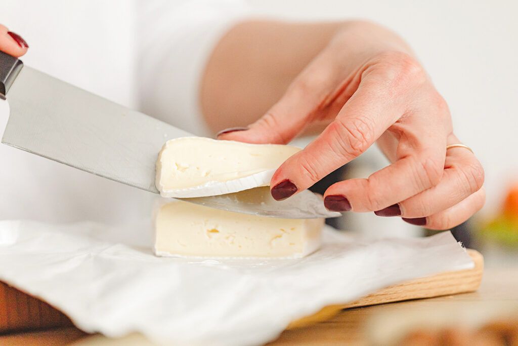 Person cutting brie cheese with knife