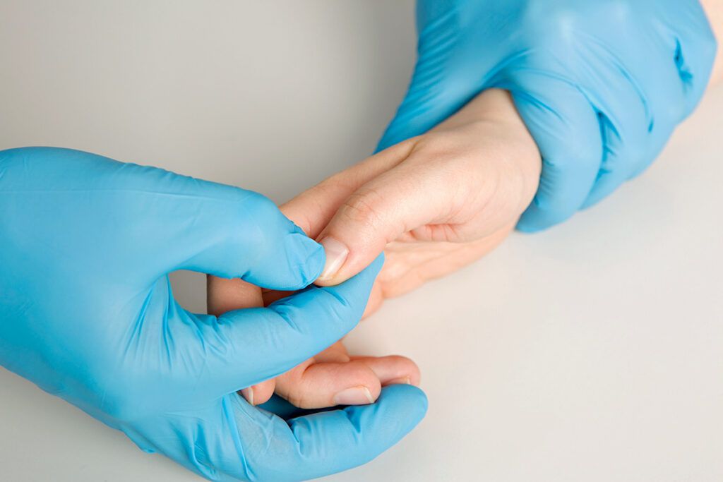 Gloved hands holding ungloved hand and pressing on nail