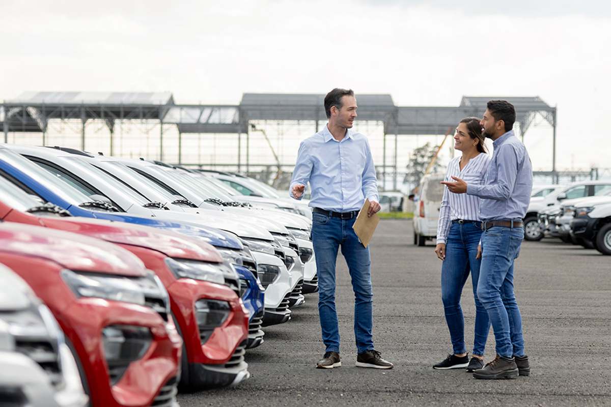 Car salesman and couple in a lot with cars