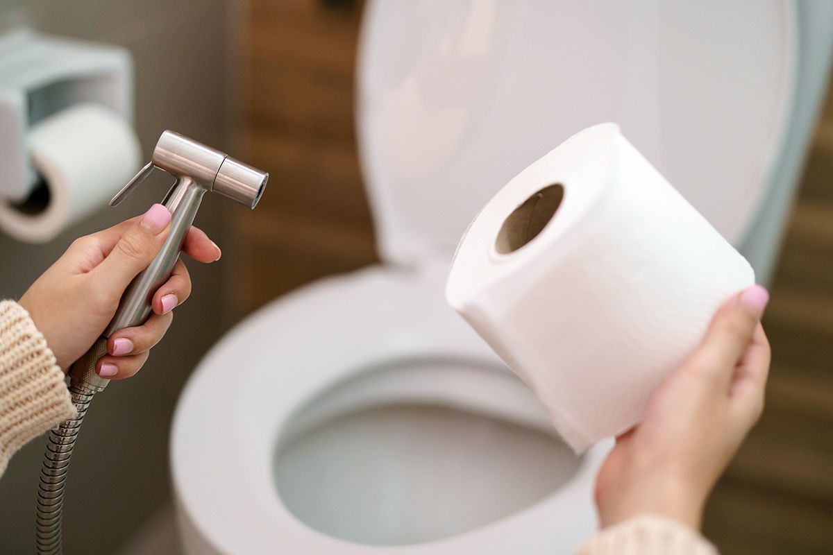 Person holding bidet nozzle and toilet paper