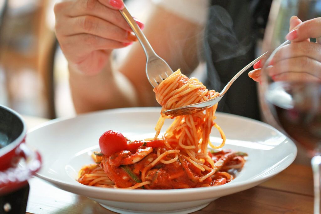 Person holding spoon and fork with spaghetti
