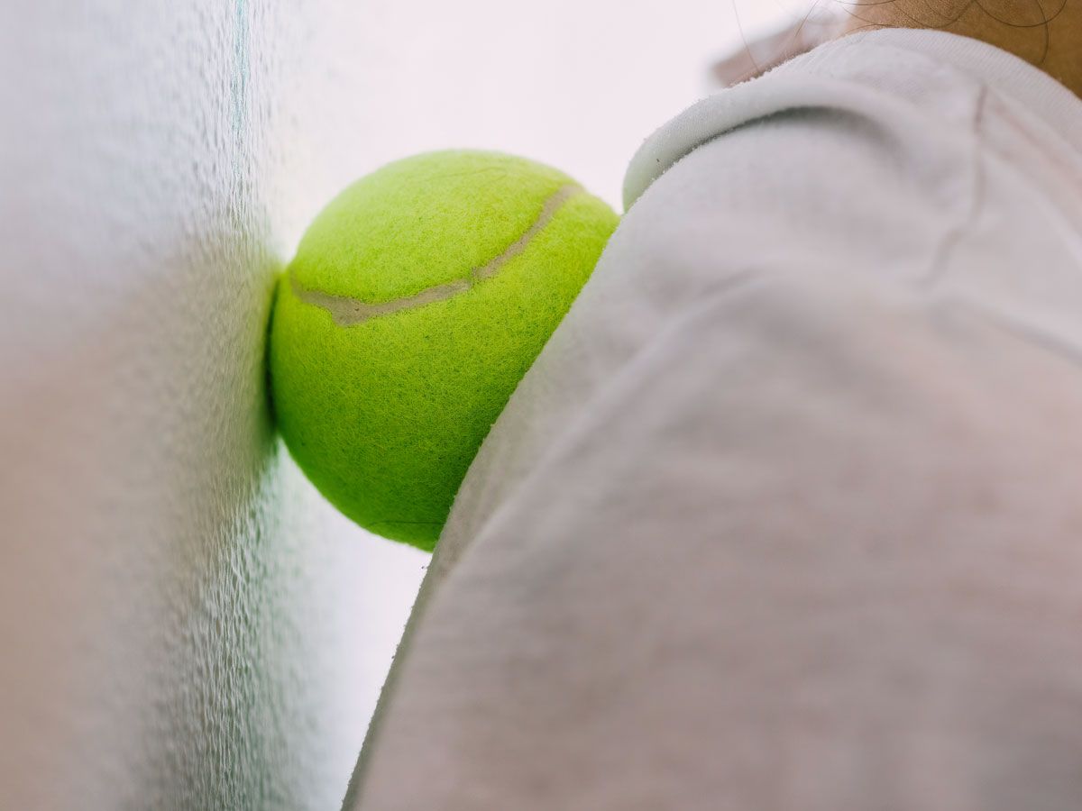 Person using tennis ball to stretch against wall