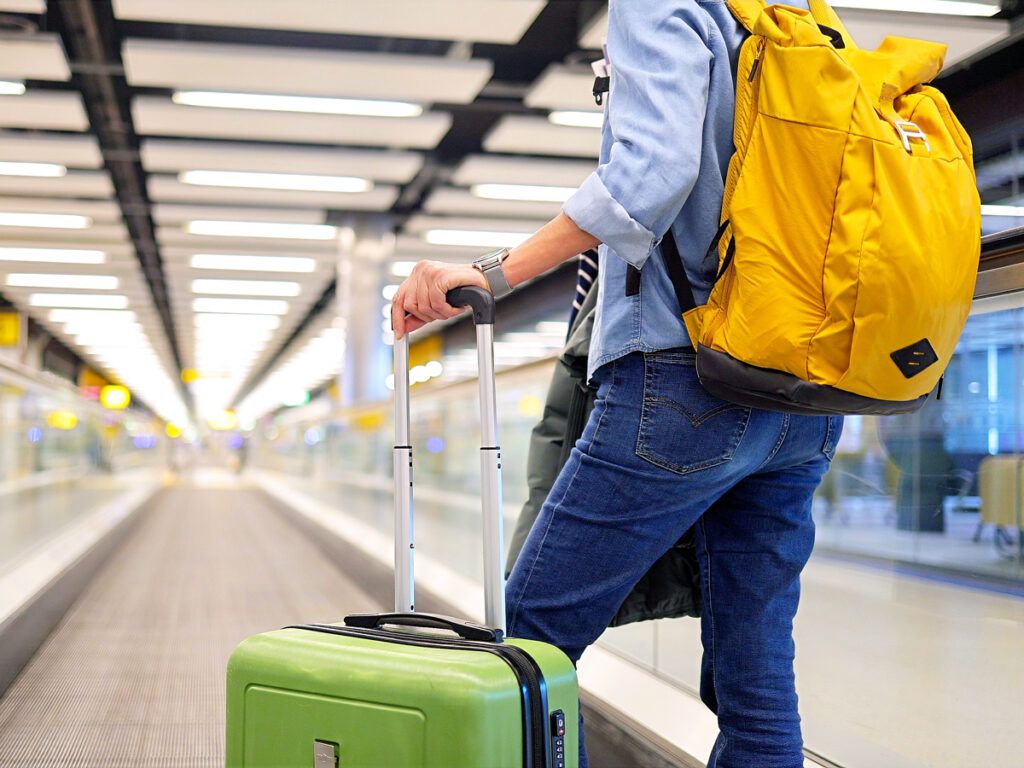 Traveler with backpack and roller luggage on moving walkway in airport