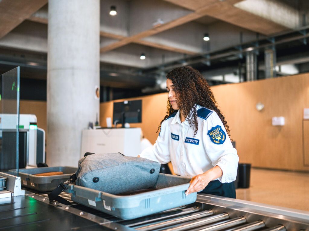 Security officer placing bin on belt for scanning