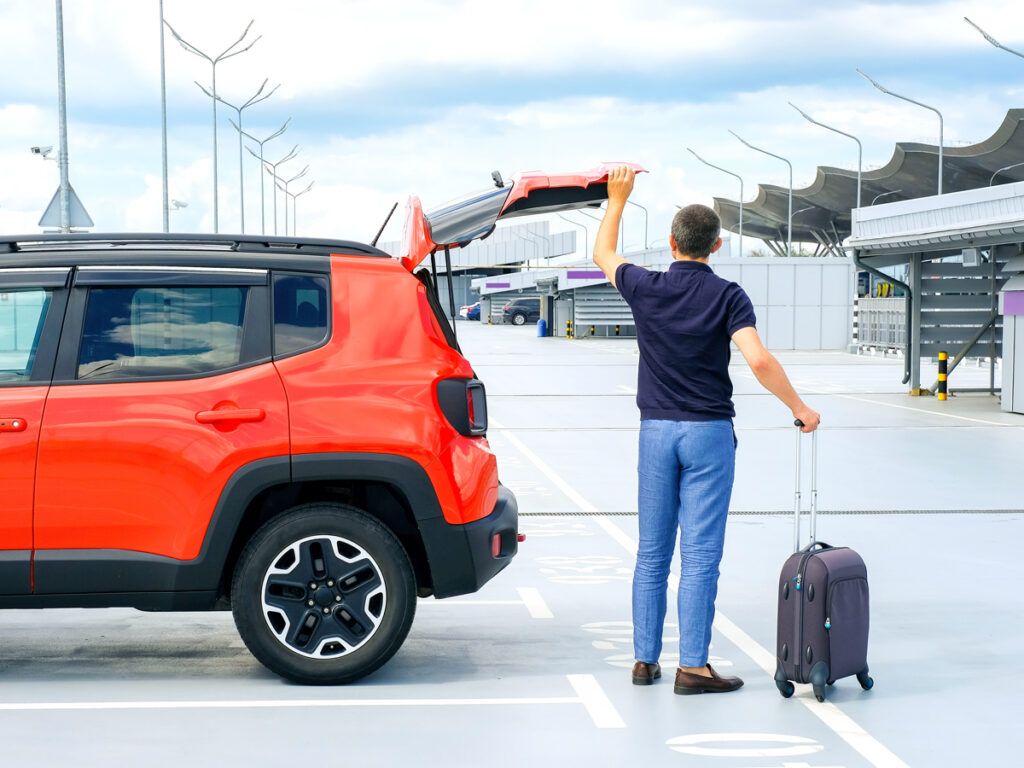 Traveler taking suitcase out of car in airport parking lot
