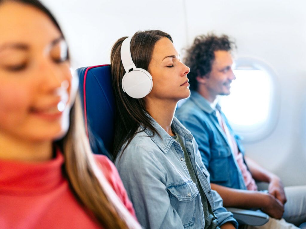 Passenger in airplane seat with eyes closed and headphones on