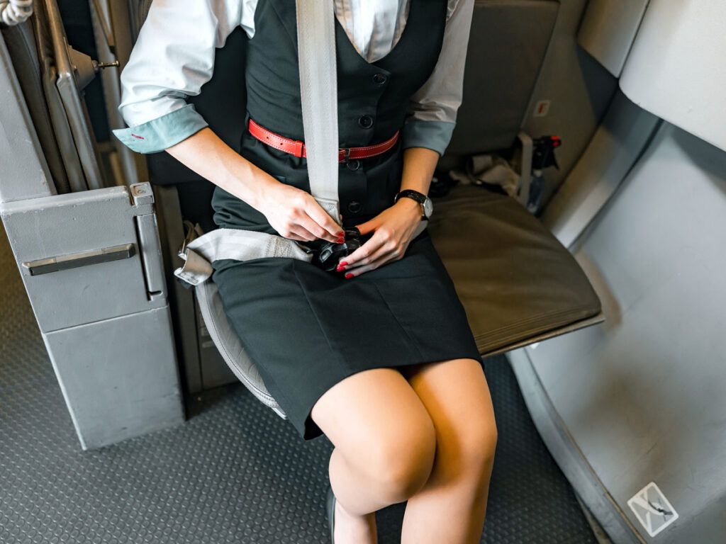 Flight attendant fastening seat belt in jump seat