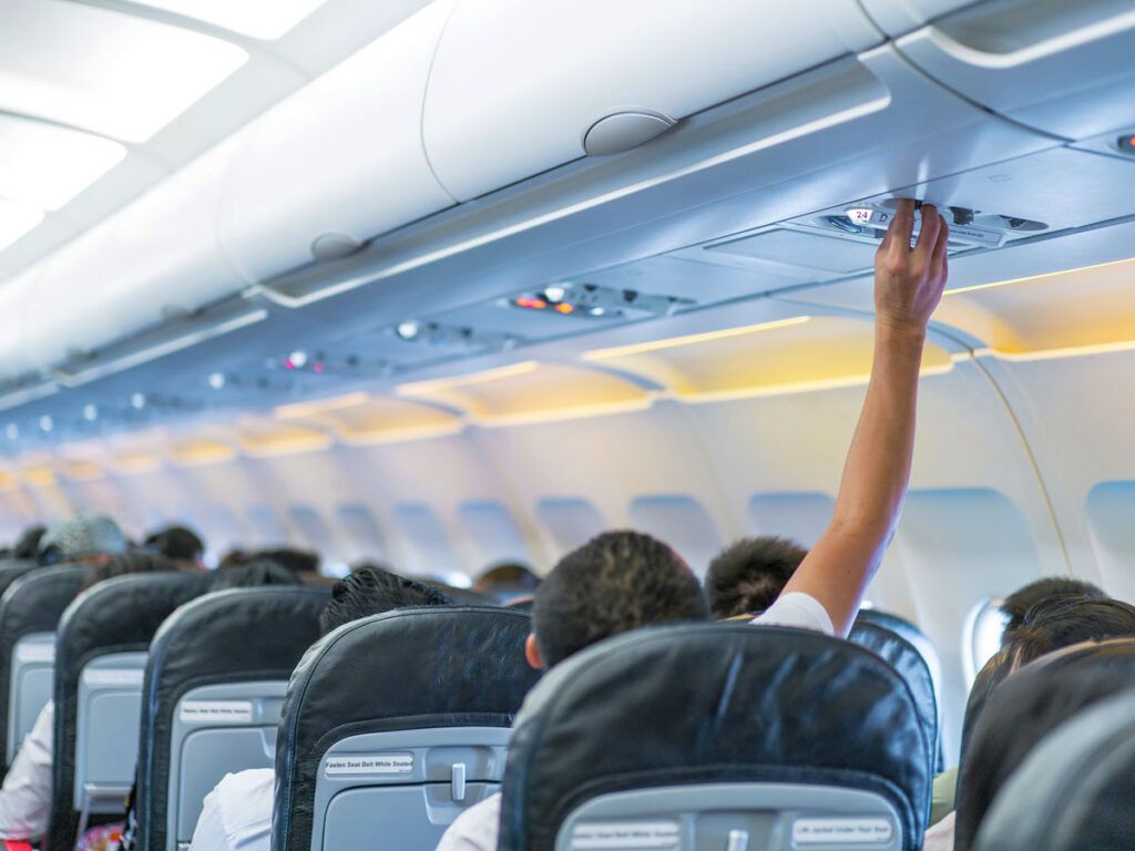 Traveler reaching for overhead air vent on airplane