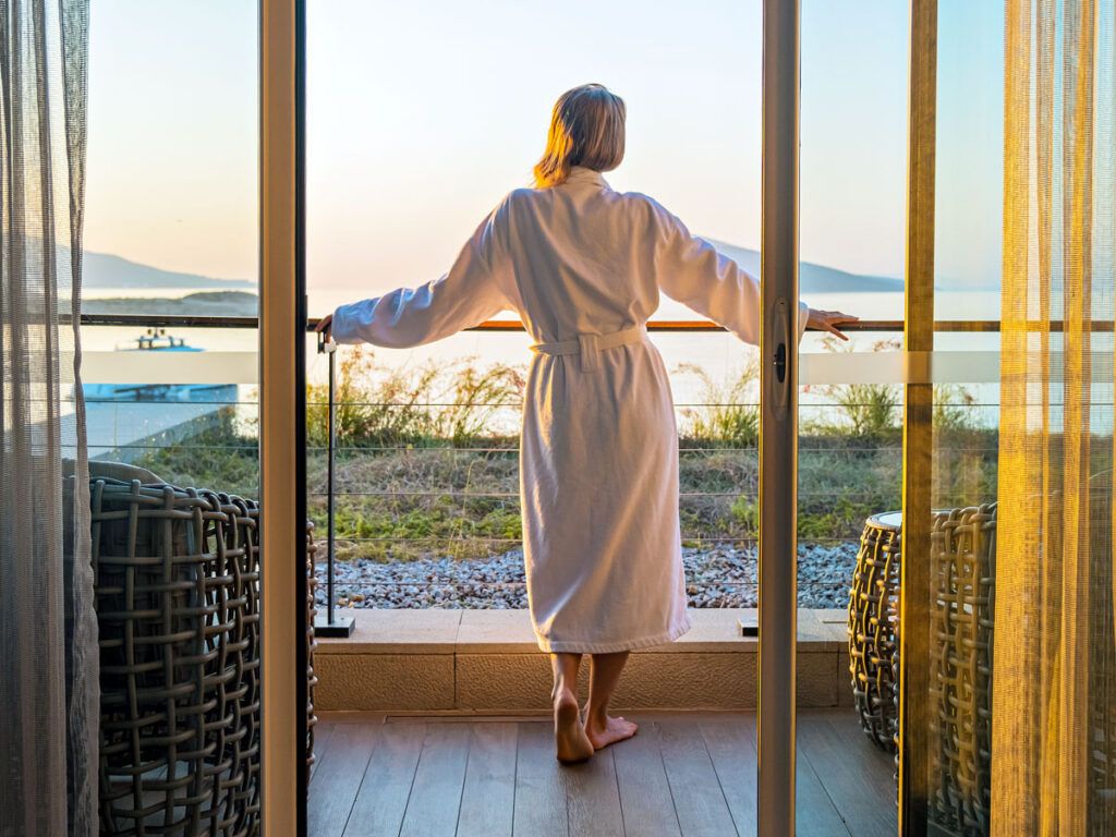 Woman standing in robe looking out over sea from hotel balcony