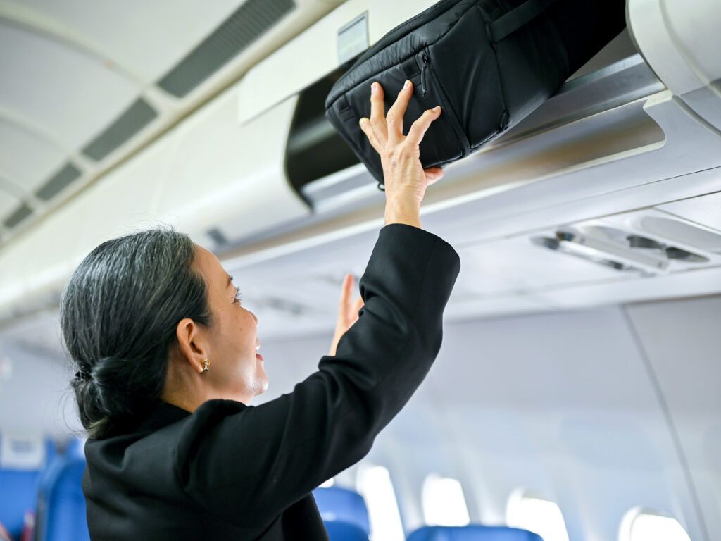 Airline passenger placing bag in overhead bin
