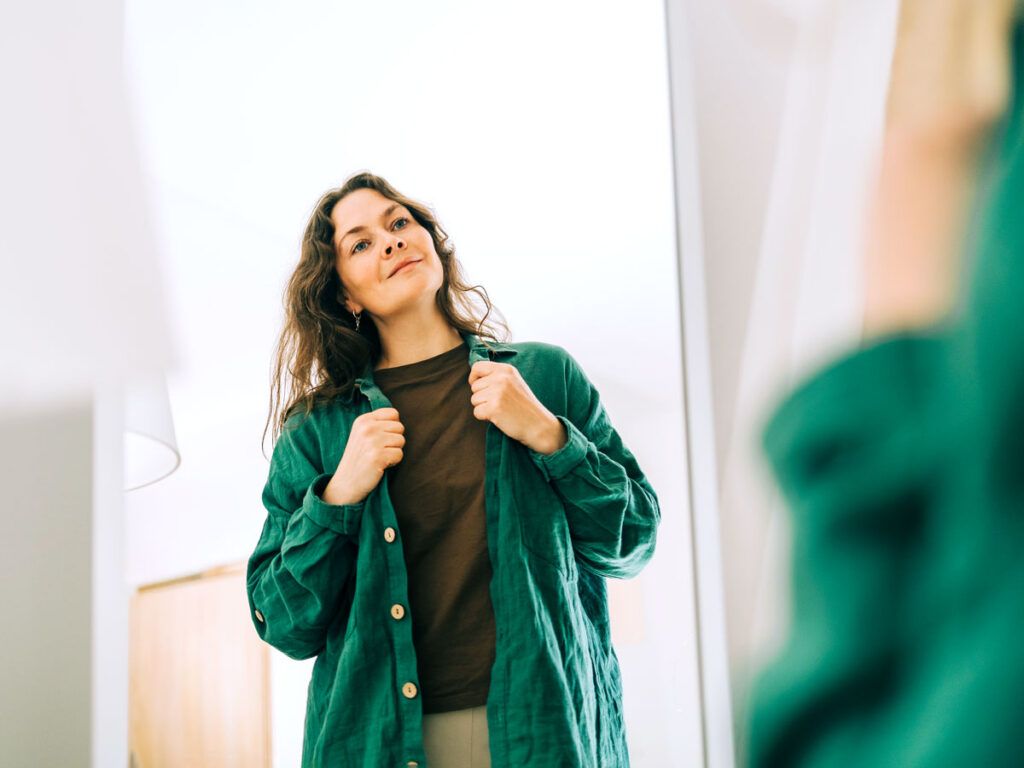 Woman trying on shirt in front of mirror