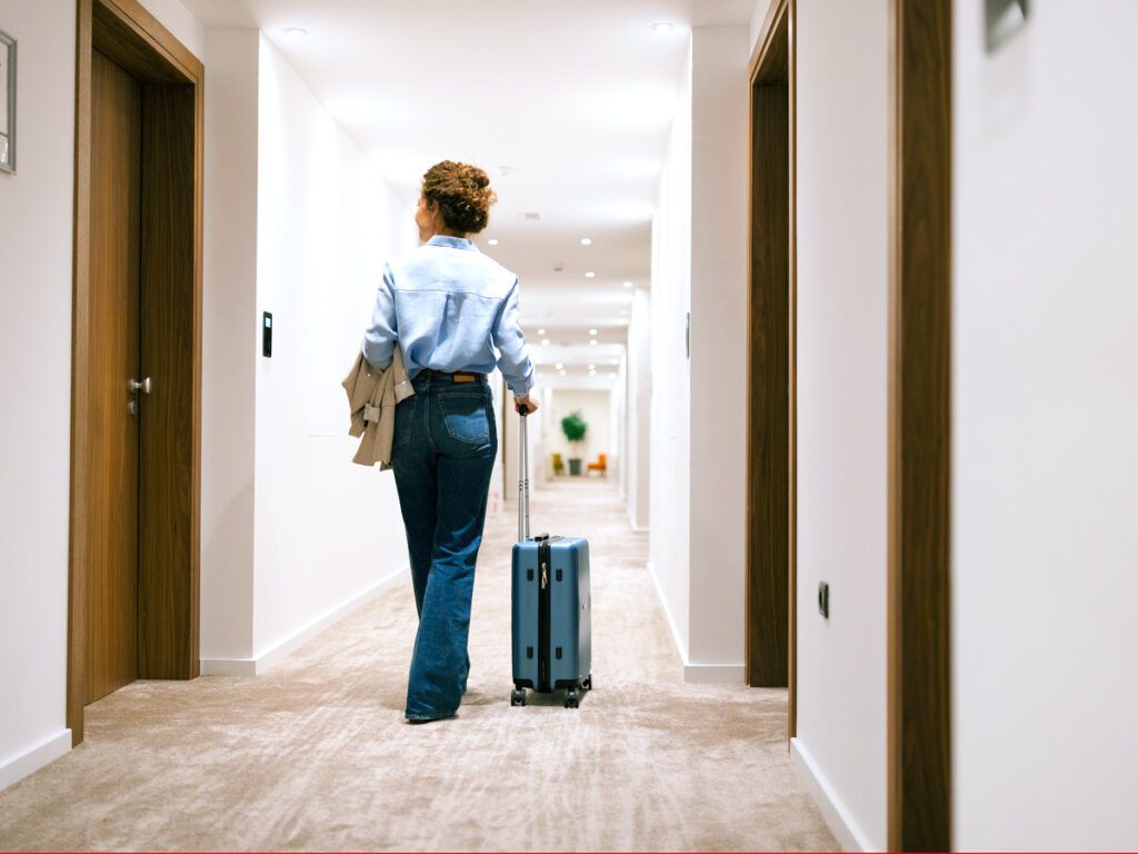 Woman walking through a hotel corridor with a suitcase
