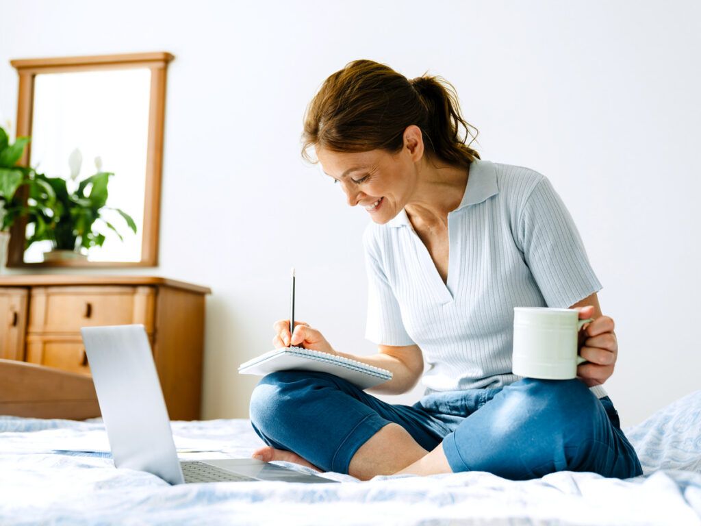 Woman writing down notes while working on a laptop