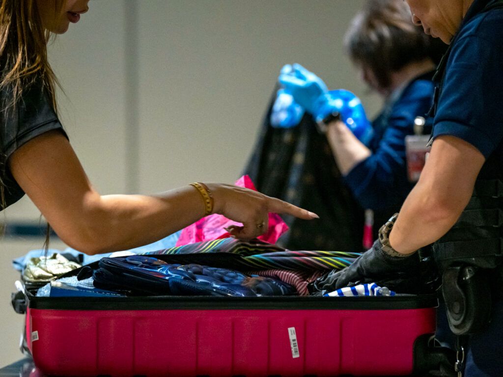 Traveler pointing out item in suitcase to security officer at airport checkpoint