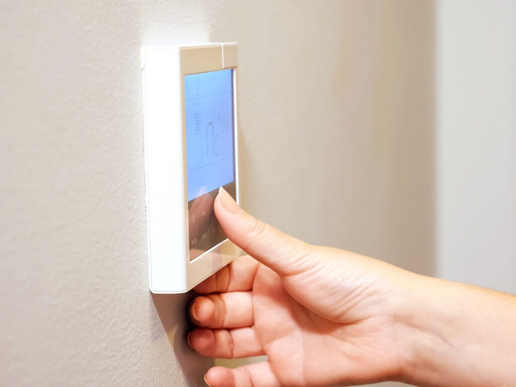 Person setting thermostat on wall
