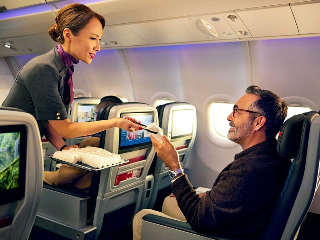 Flight attendant handing passenger a hot towel in premium economy