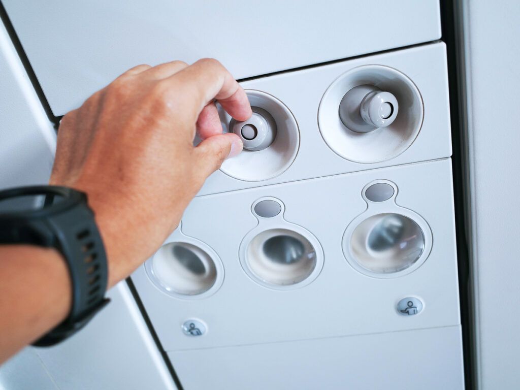 Passenger adjusting air nozzle on overhead unit