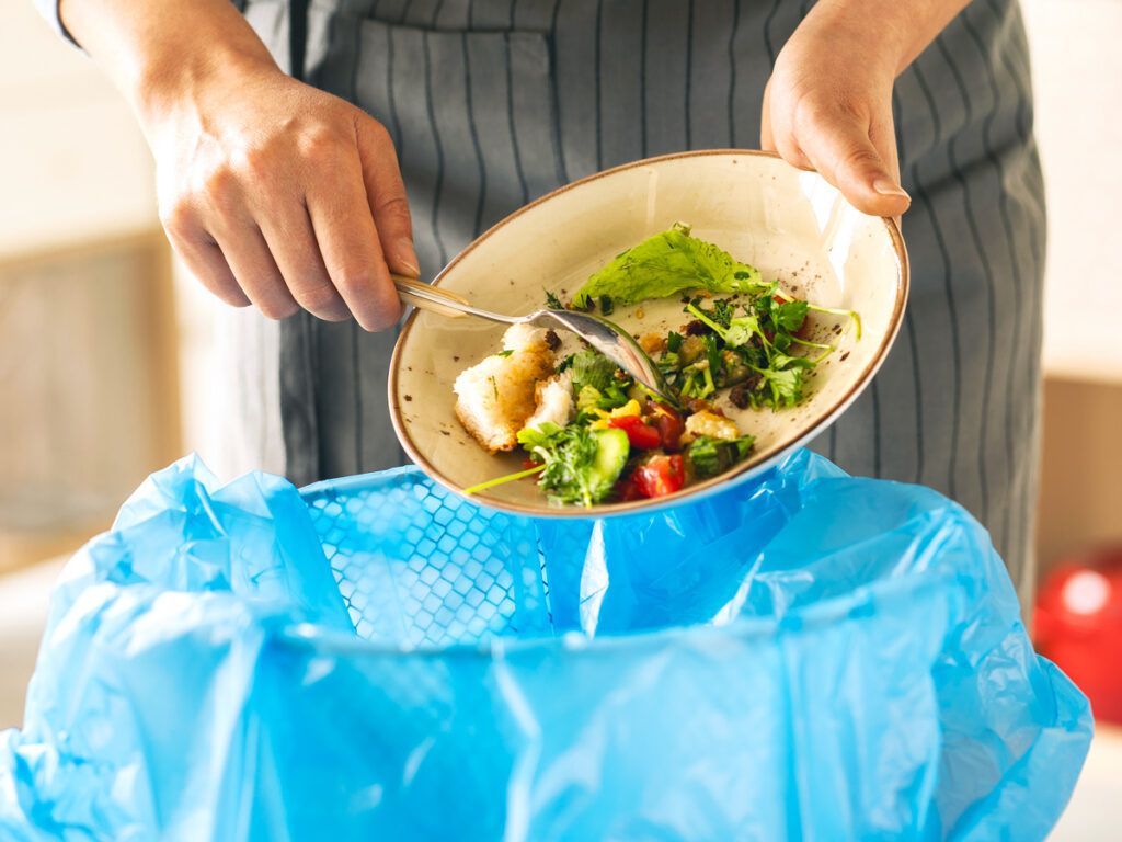 Woman scraping the leftover food from her plate into the trash bin