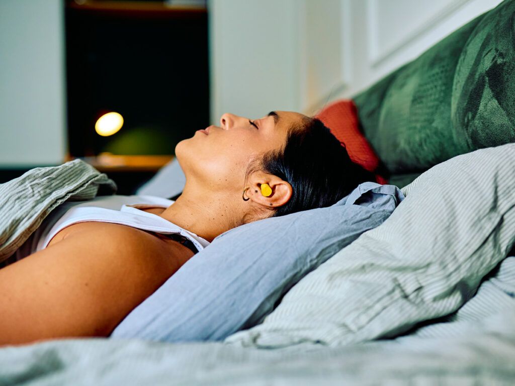Woman wearing earplugs while relaxing in bed