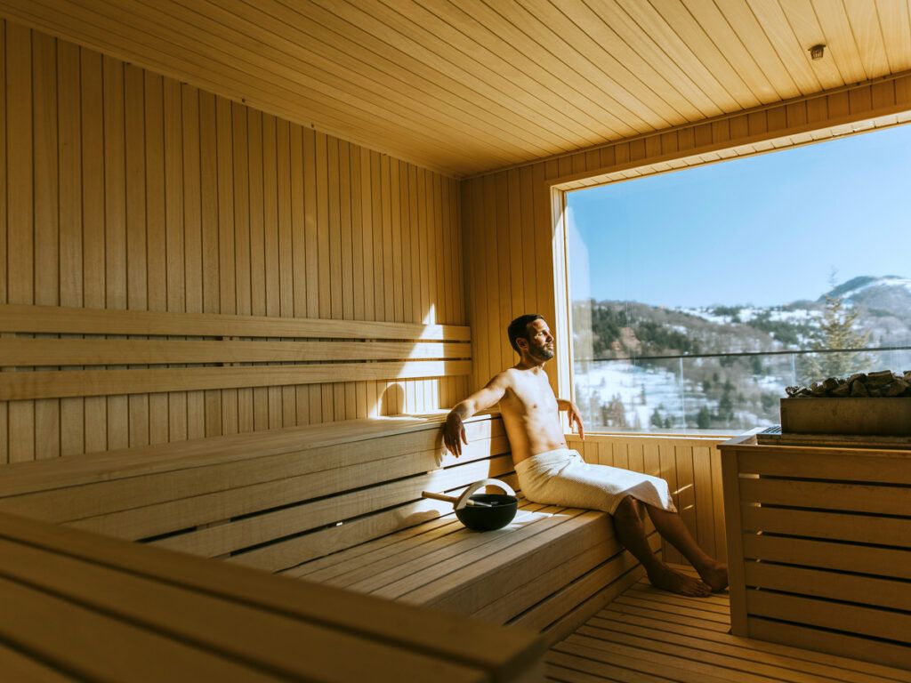 Man relaxing in the sauna and enjoying the forest through a window