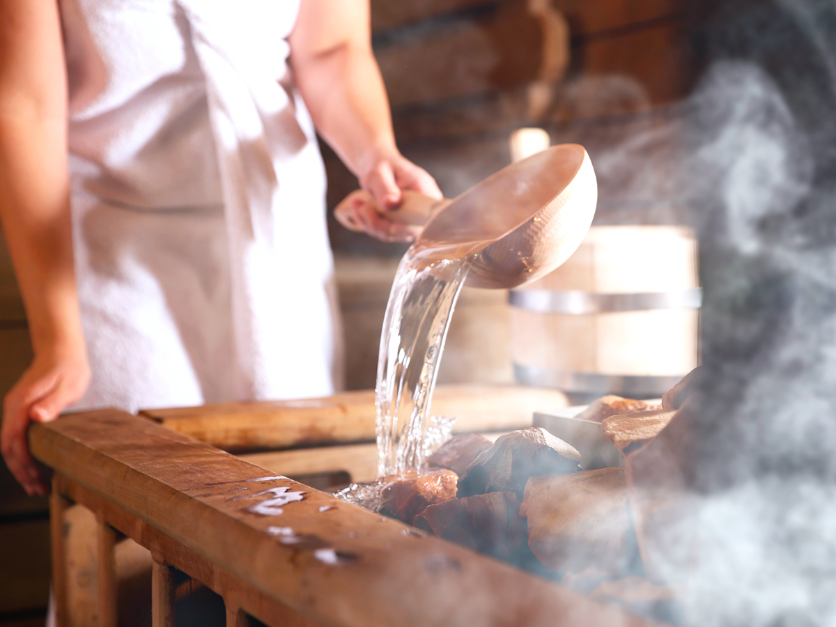 Woman pouring water onto stones in sauna
