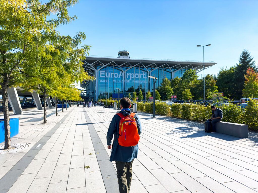 Man with a red backpack walking toward EuroAirport Basel-Mulhouse-Freiburg