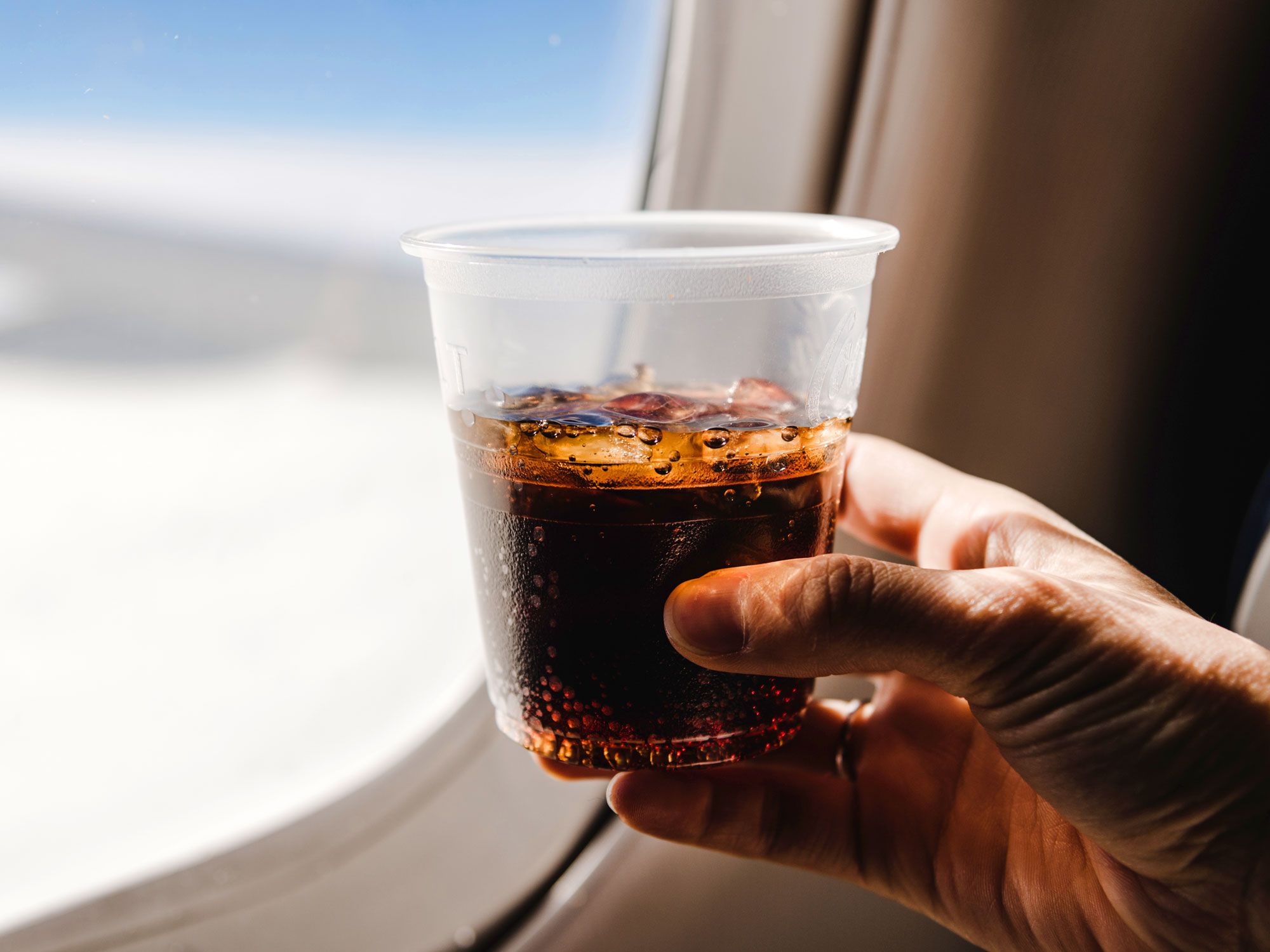 Passenger holding cup of soda by plane window